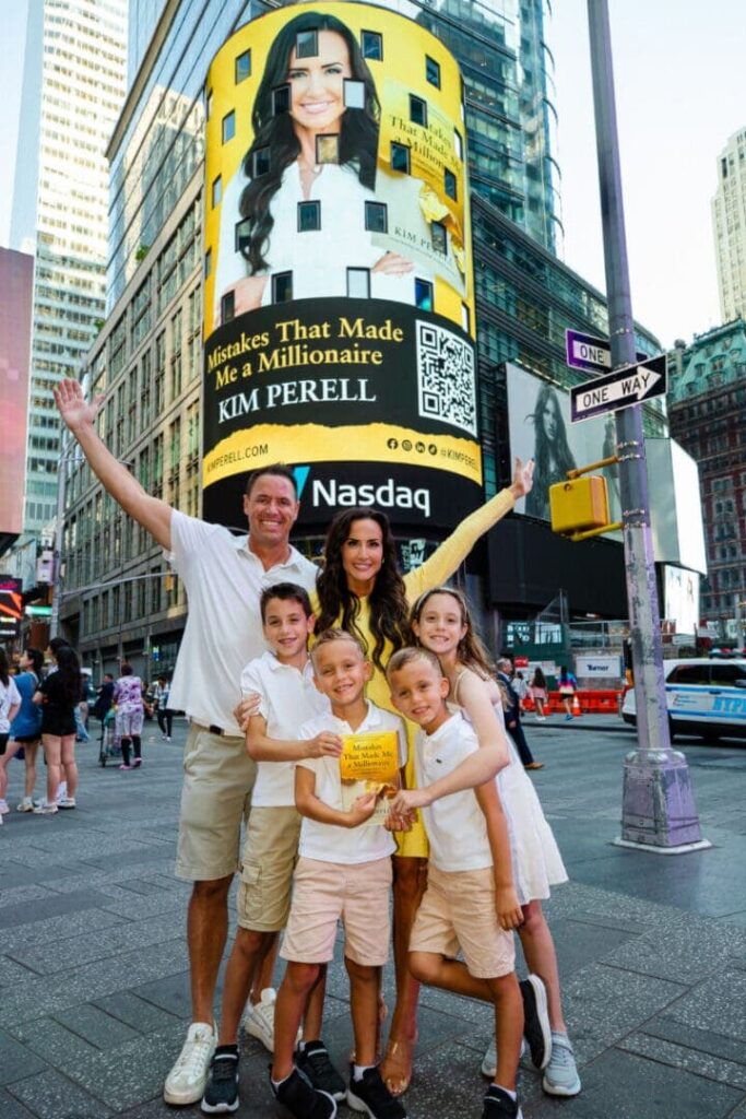 Family celebrating in front of a large digital billboard featuring Kim Perell's advertisement for "Mistakes That Made Me a Millionaire" in Times Square, New York City.