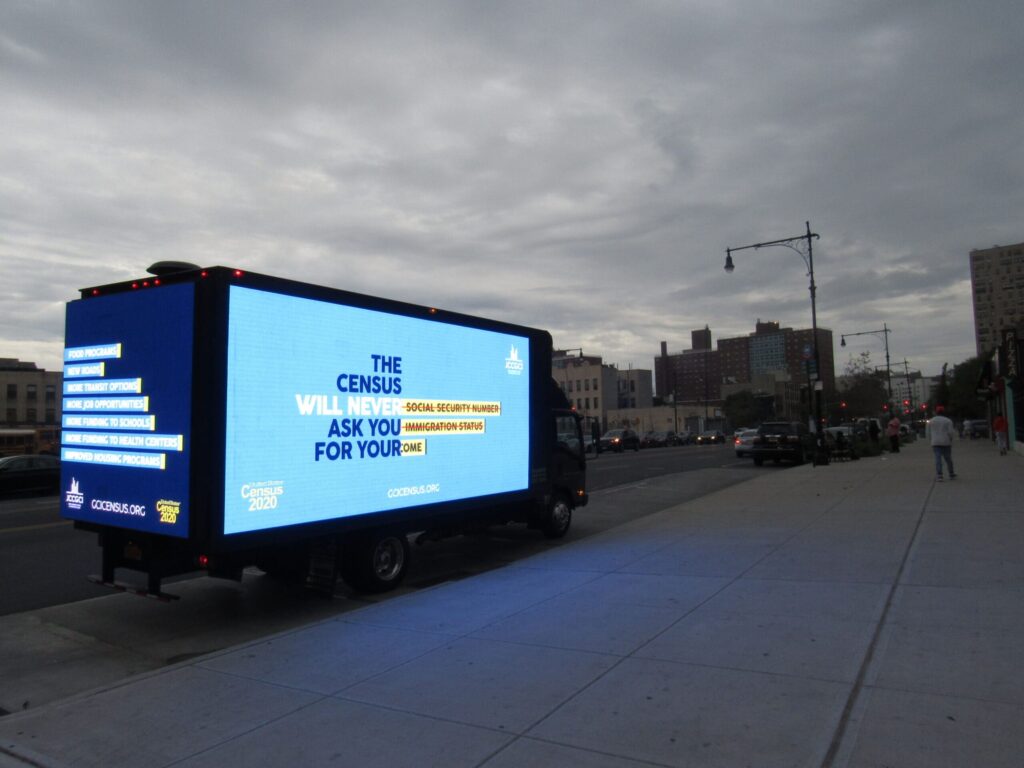 Truck with illuminated census advertisement at dusk.