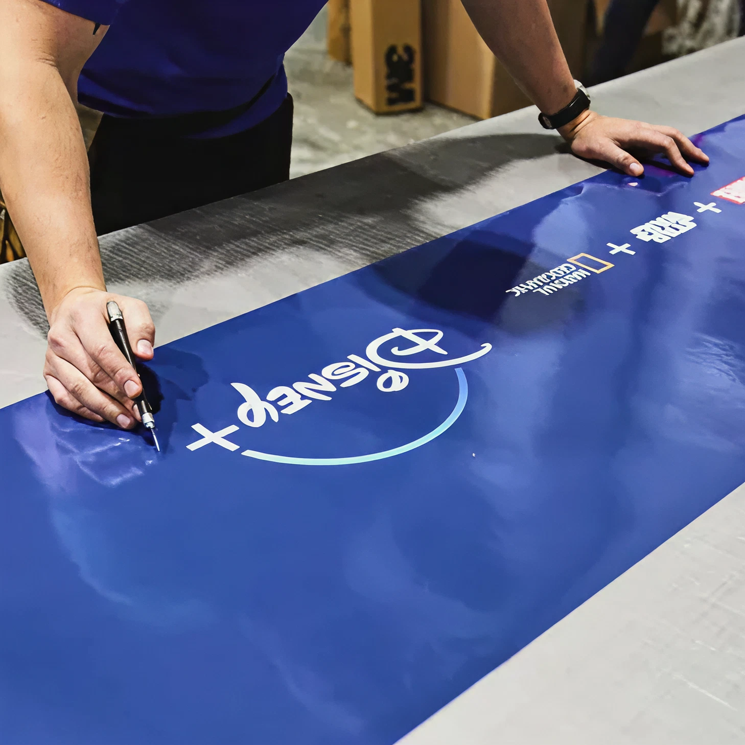 Person signing a blue promotional banner with the Disney+ logo, emphasizing branding for advertising campaigns in Maine.