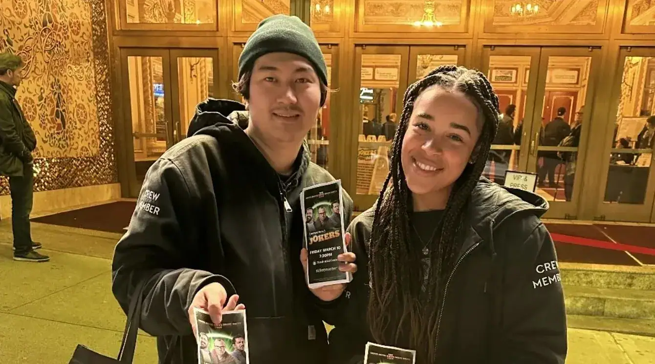 Two street team members holding promotional flyers in front of a venue, showcasing American Guerrilla Marketing's flyer distribution strategy.