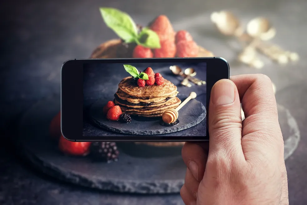 Person photographing a stack of pancakes topped with strawberries and honey, highlighting food photography for content creation and SEO marketing.