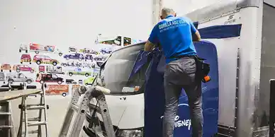 Man applying vehicle wrap on a truck for advertising, showcasing the transformation of vehicles into mobile billboards in a marketing setting.