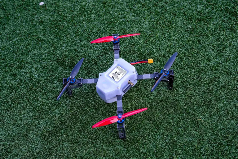 Drone on green turf, featuring red propellers and a white body, representing technology used in American Guerrilla Marketing's innovative drone light shows for events.