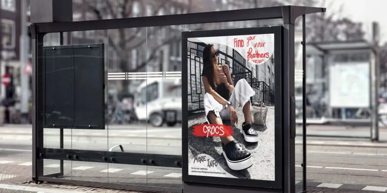 Bus stop advertising featuring a Crocs advertisement with a model wearing white pants and black shoes, promoting the message "Find your perfect pair."