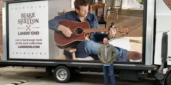 Blake Shelton promoting Lands' End on a mobile billboard truck, featuring him playing guitar with a cozy indoor setting in the background.