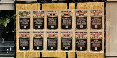 Newport Jazz festival promotional posters arranged in a grid on a wooden wall, featuring event details and QR codes, showcasing guerrilla marketing strategies for arts events.