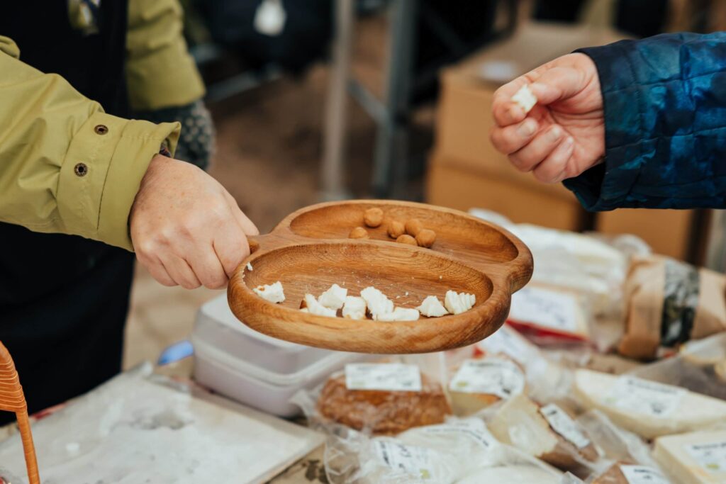 Hands offering cheese samples at market stall.