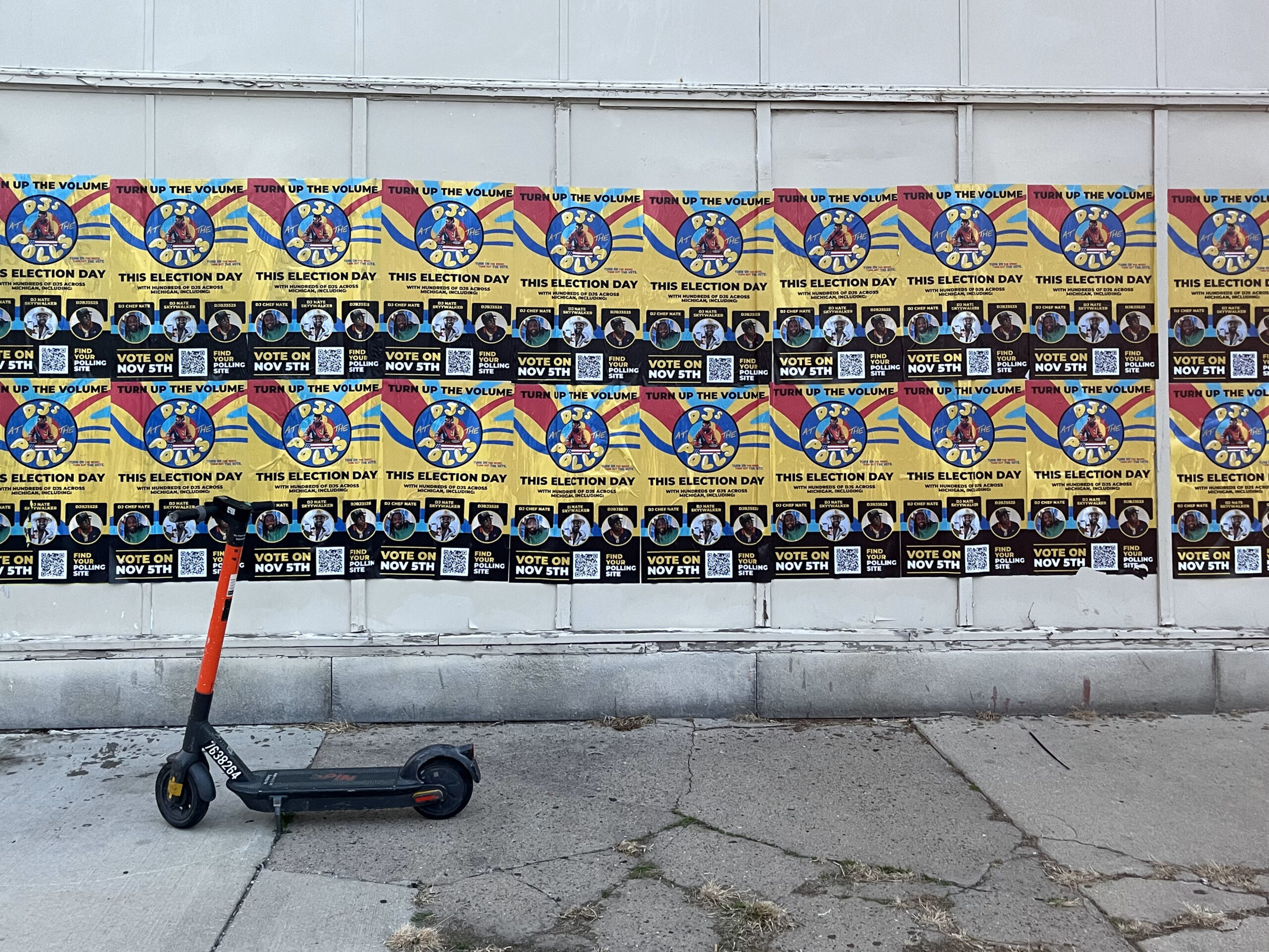 Wall covered with vibrant wild wheat paste posters promoting an election, featuring the message "Vote on Nov 8th," alongside a parked scooter, illustrating guerrilla marketing in urban Arkansas.