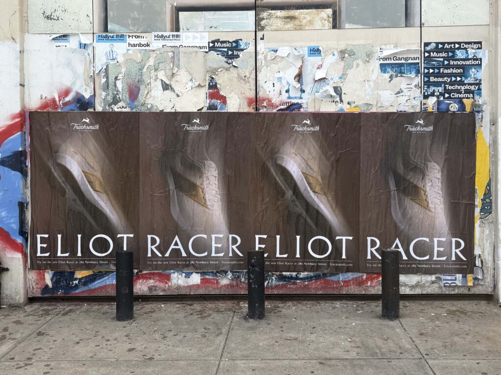 Posters featuring "Eliot Racer" prominently displayed on a weathered wall, showcasing urban street marketing and advertising strategies.