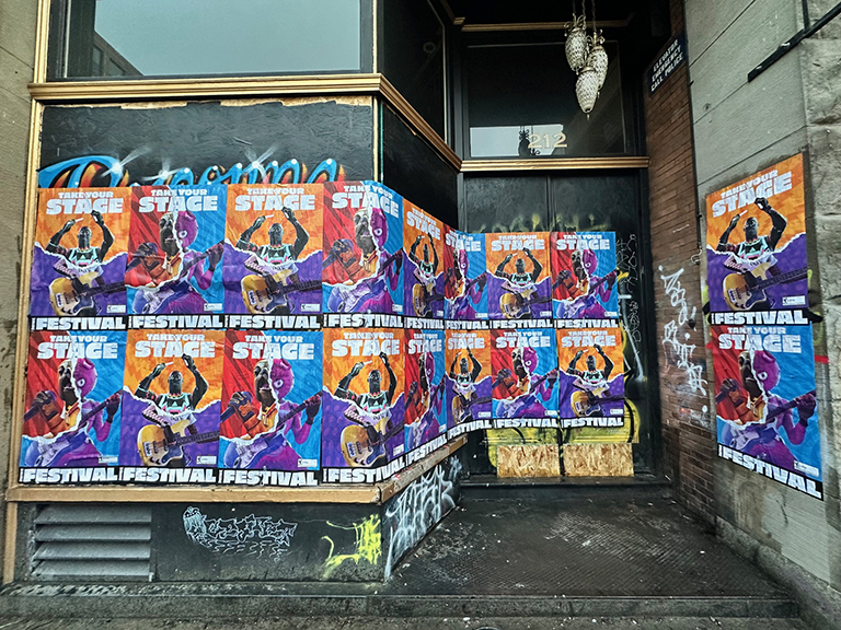 Wild wheat paste posters advertising a festival covering a storefront in an urban setting, showcasing vibrant colors and artistic designs, reflecting guerrilla marketing strategies in Montana.