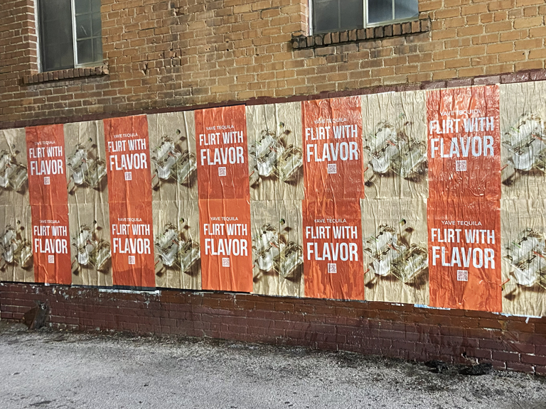 Wild wheat paste posters on a brick wall in Nevada featuring the phrase "Flirt with Flavor" promoting a tequila brand, showcasing guerrilla marketing tactics.
