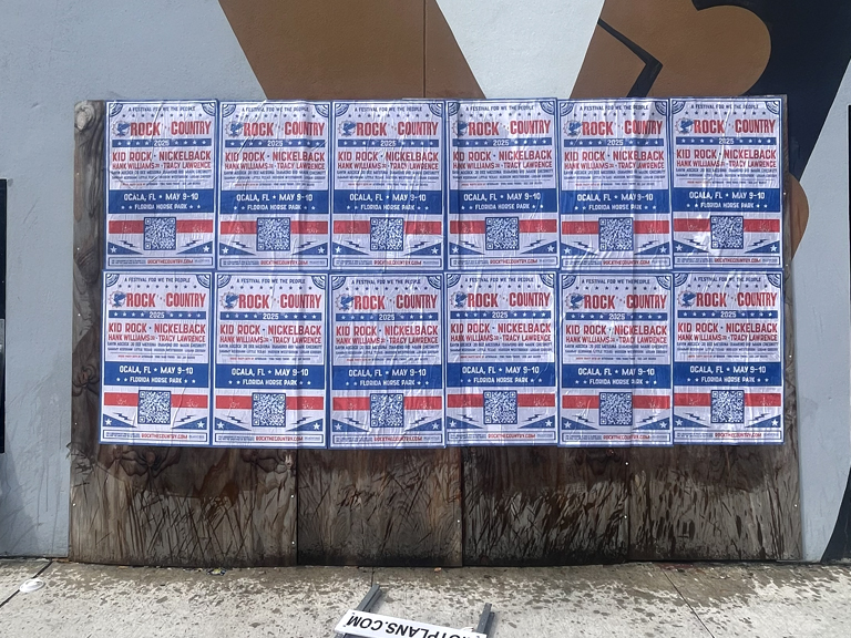 Wild wheat paste posters advertising a concert featuring Kid Rock and Nickelback, displayed on a wooden board in an urban setting, showcasing guerrilla marketing tactics in North Dakota.