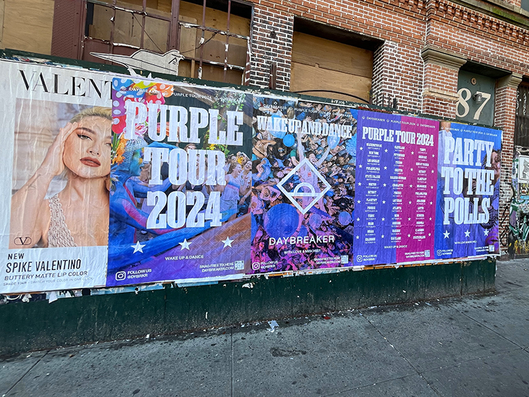 Wild wheat paste posting advertisement featuring vibrant promotional posters for the "Purple Tour 2024," showcasing artist images and event details, illustrating guerrilla marketing tactics in urban Pennsylvania settings.
