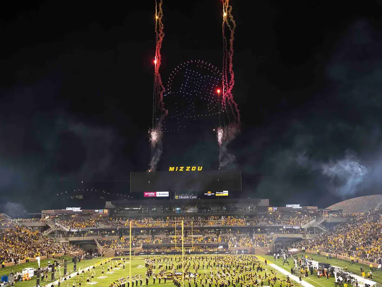 Drone light show with fireworks over Mizzou stadium, featuring a large audience and vibrant aerial displays, emphasizing innovative advertising and event engagement.
