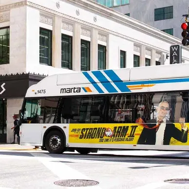 Bus advertising featuring a promotional wrap for "Strong Arm II" on a MARTA bus in an urban setting, showcasing guerrilla marketing strategies in public transit advertising.