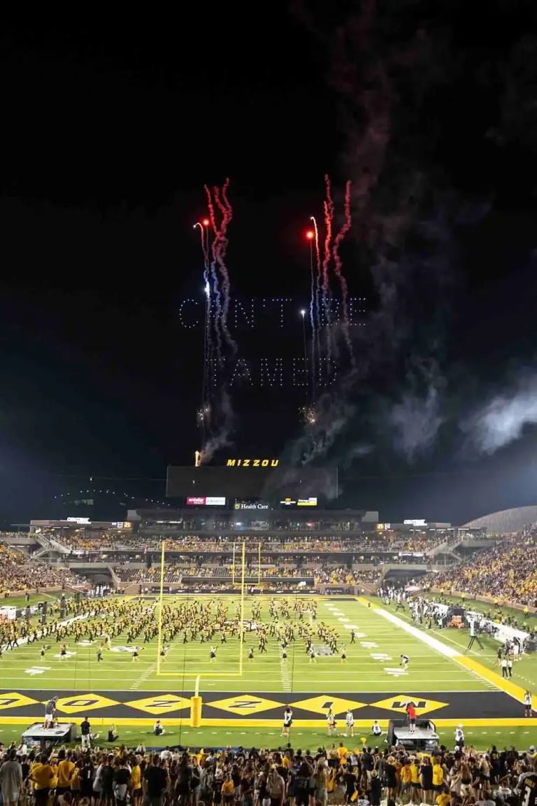 Drone light show at Mizzou stadium featuring aerial displays and fireworks, with a crowd watching below.