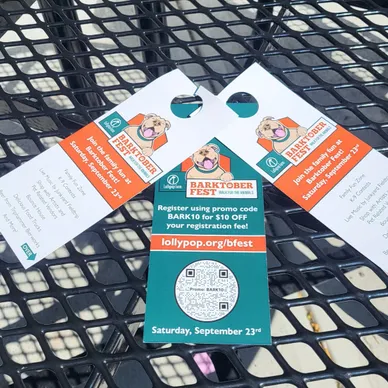 Door hangers promoting Barktober Fest event with registration details and QR code on a black table surface.