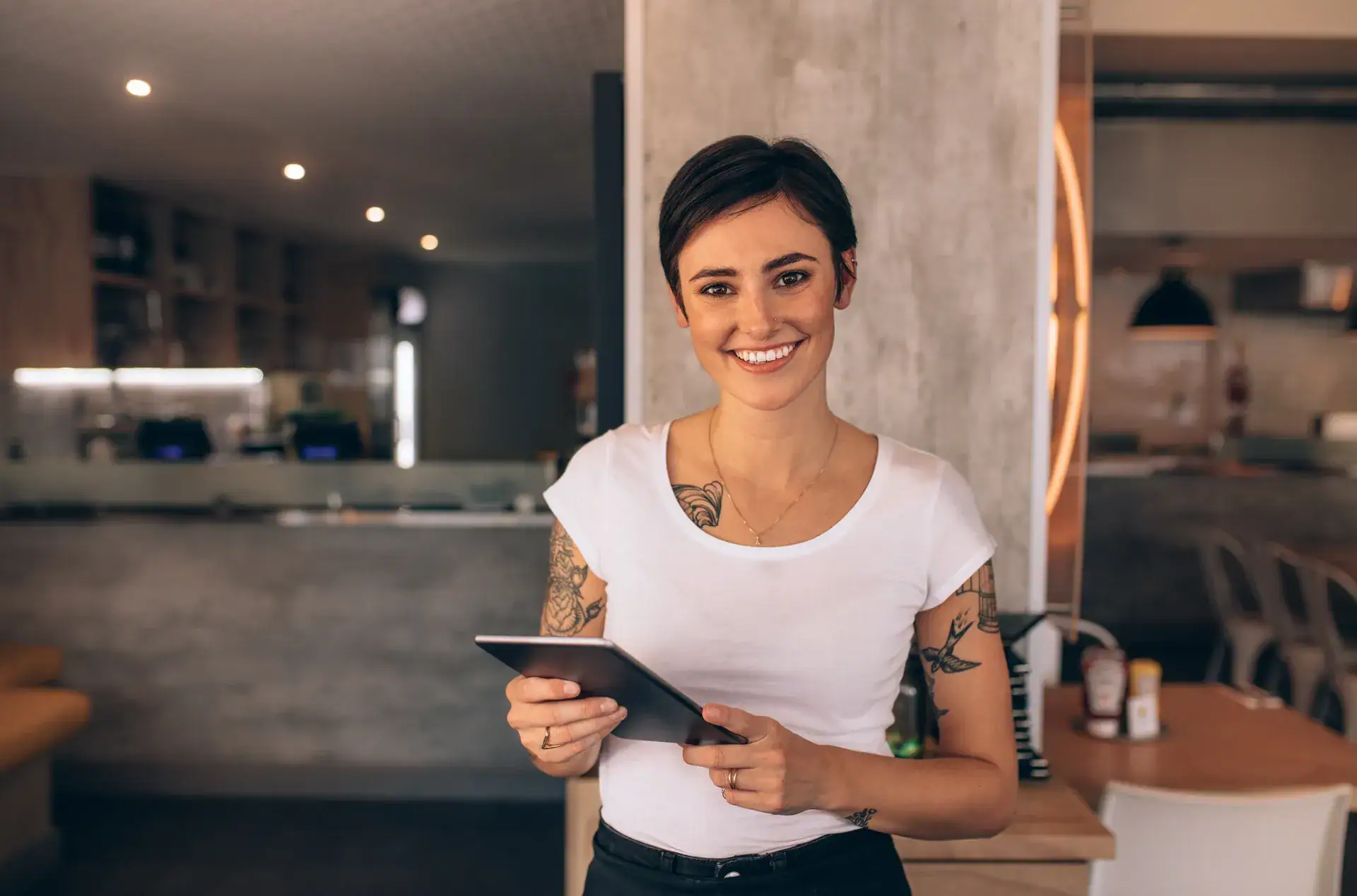 Smiling female server holding a tablet in a modern restaurant interior, showcasing customer service in the hospitality industry.