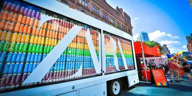 Colorful beverage truck displaying stacked cans in a rainbow arrangement, promoting a vibrant marketing campaign at an outdoor event.