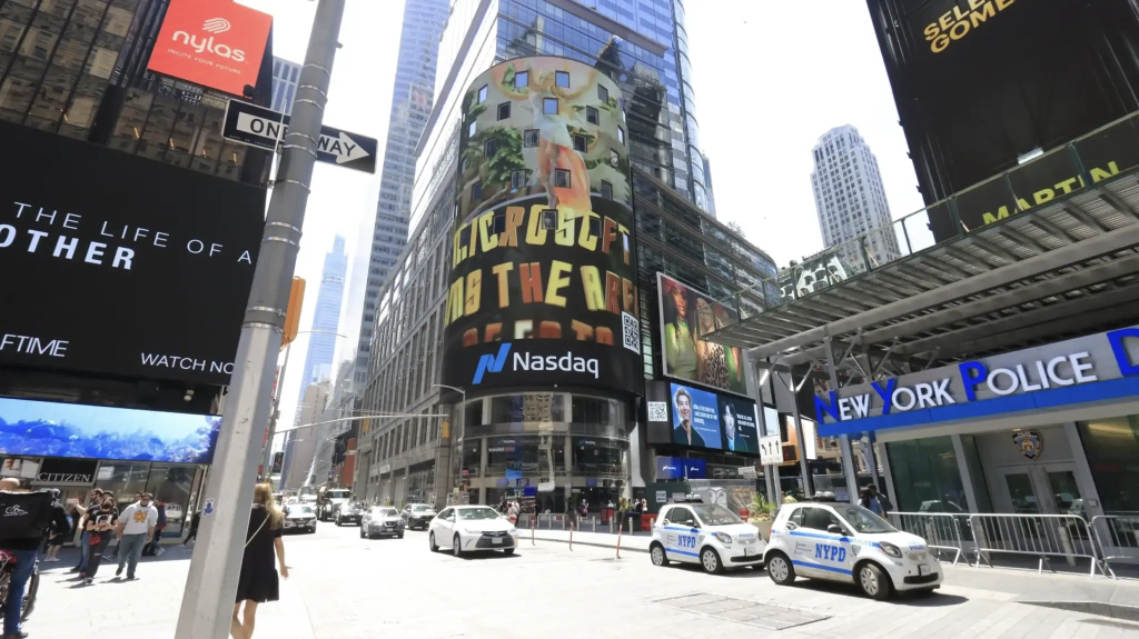 Billboard advertisement featuring Nasdaq logo and vibrant artwork in Times Square, Manhattan, surrounded by busy traffic and pedestrians.
