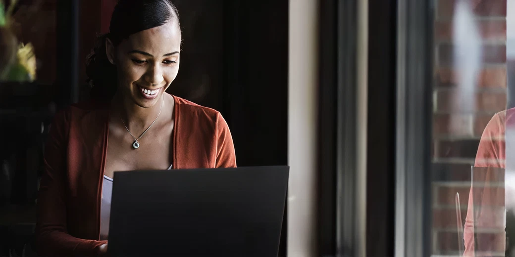 Smiling woman engaging with a laptop, representing content creation and digital marketing strategies for enhancing online presence.