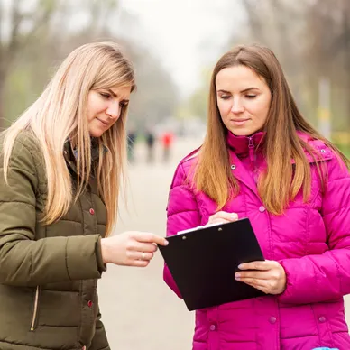 Two women discussing survey results while reviewing a clipboard outdoors, representing nationwide street surveys for guerrilla marketing strategies.