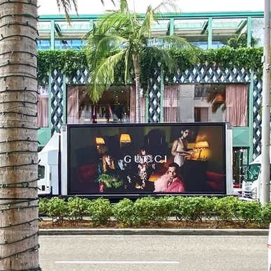 LED billboard truck displaying a Gucci advertisement in an urban setting, surrounded by palm trees and modern architecture, highlighting innovative guerrilla marketing strategies.