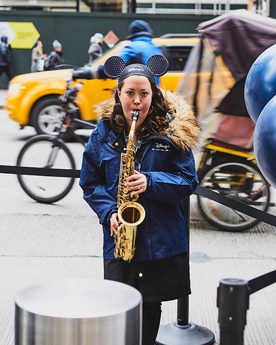 Musician wearing Mickey Mouse ears playing saxophone in urban setting, promoting pop-up marketing experiences.
