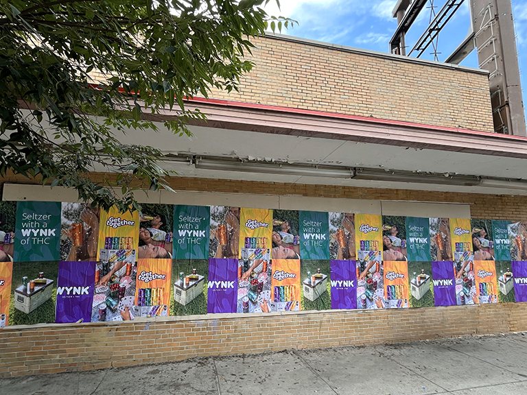 Colorful outdoor advertising display featuring WYNK cannabis-infused seltzer posters on a storefront wall, promoting compliance with cannabis marketing regulations.