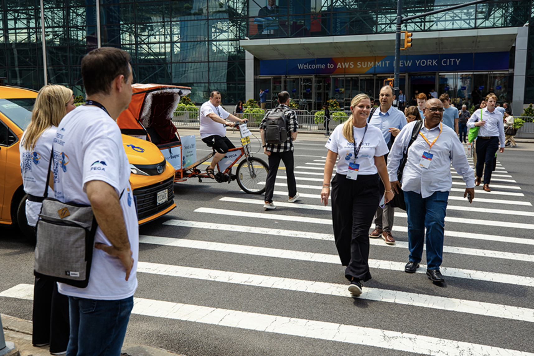 Crowd of professionals walking across a crosswalk near an event venue, with a bicycle rickshaw and taxis, showcasing interactive marketing and brand activation at a conference.