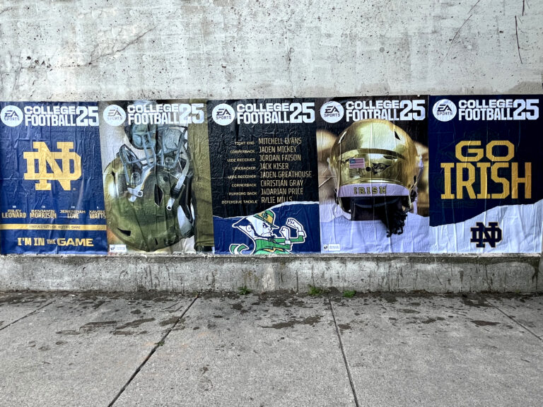 EA Sports College Football 25 promotional posters featuring Notre Dame branding, player names, and imagery, displayed on a concrete wall, highlighting guerrilla marketing strategy targeting college campuses.