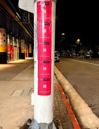Wheatpaste poster advertising on a street pole featuring vibrant pink flyers with QR codes, promoting sports marketing services and brand engagement strategies in urban environments.