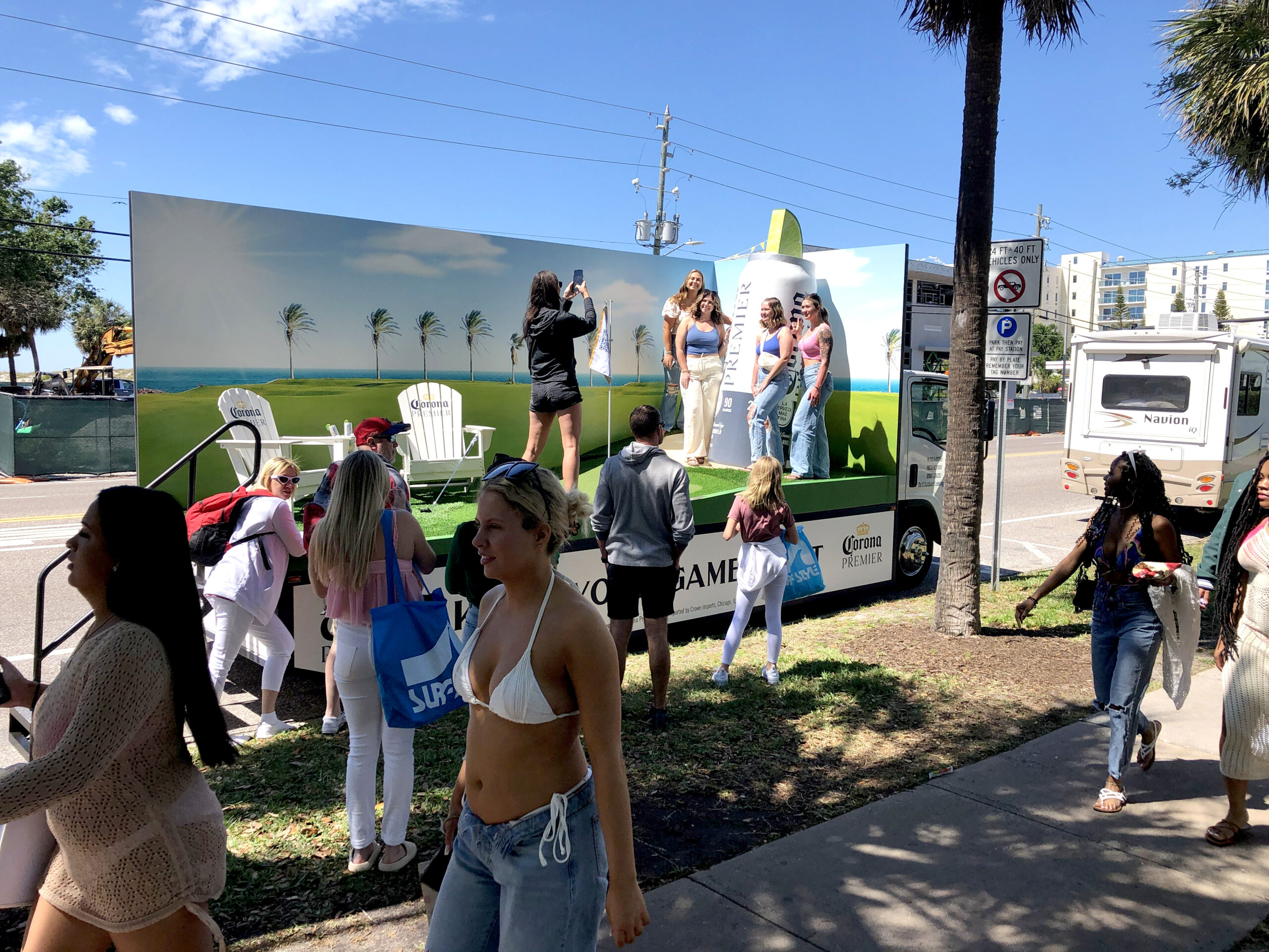 Crowd interacting with a branded mobile marketing activation featuring a photo opportunity, promoting experiential marketing with people posing in front of a truck displaying a beach scene.