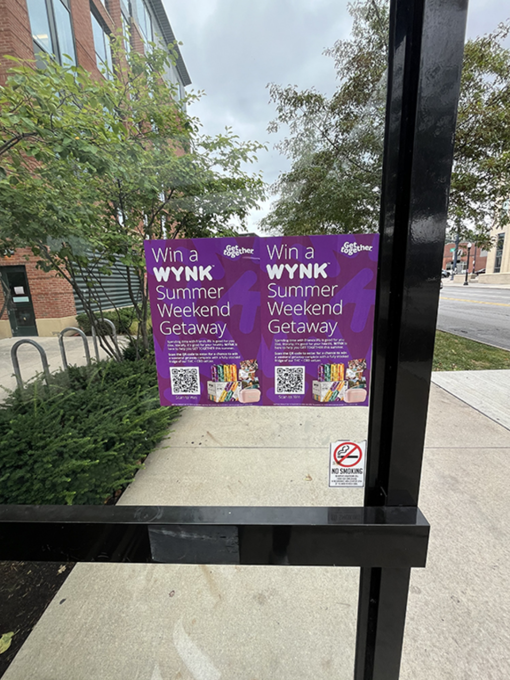 Win a WYNK Summer Weekend Getaway promotional poster displayed on a bus shelter, featuring vibrant colors and QR codes for engagement, relevant to outdoor guerrilla advertising strategies for cannabis marketing.