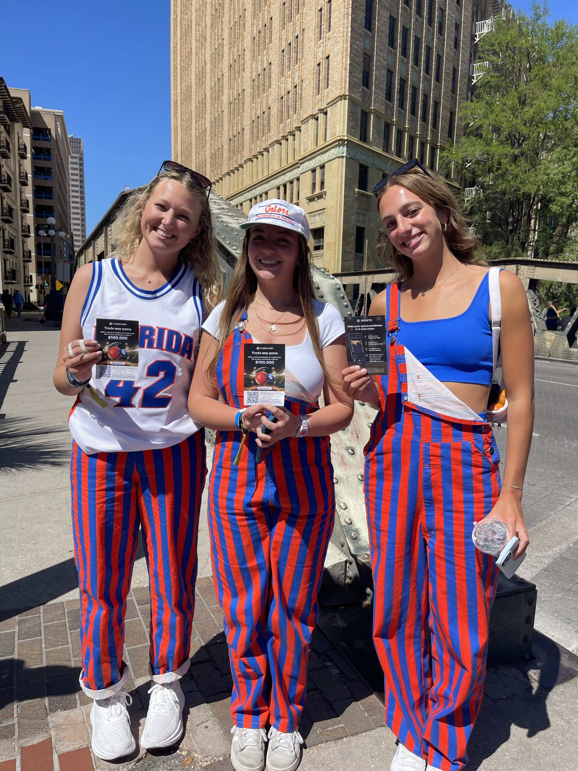 Three brand ambassadors in colorful striped outfits holding promotional flyers, smiling in an urban setting, showcasing engagement for a marketing campaign.