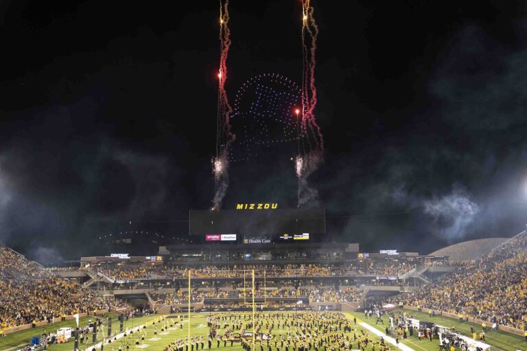 Mizzou halftime drone show with 300 drones creating formations above a stadium, synchronized fireworks, and Marching Mizzou band performing in front of a large audience.