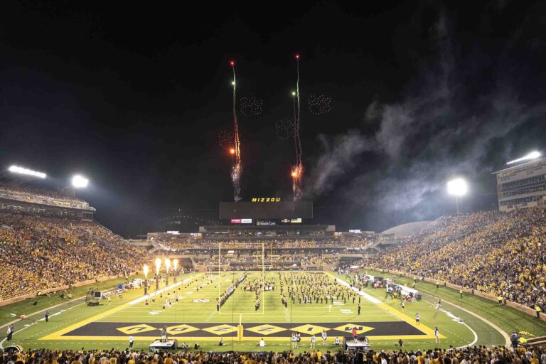Mizzou halftime drone show featuring fireworks, marching band, and illuminated stadium, showcasing athletic iconography and vibrant audience engagement.