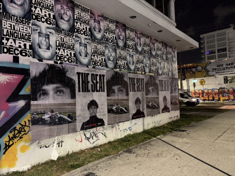 Wheatpasted posters promoting Netflix's "The Seat" campaign, featuring large images of drivers and bold text, displayed on a wall in a high-traffic Miami area during the F1 weekend, creating a cinematic effect for event attendees.