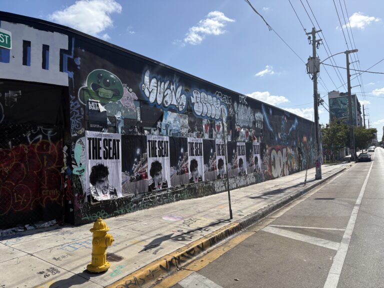 Wheatpasted posters for Netflix's "The Seat" campaign on a graffiti-covered wall in Miami, showcasing a cinematic design in a high-traffic area during the F1 Grand Prix weekend.