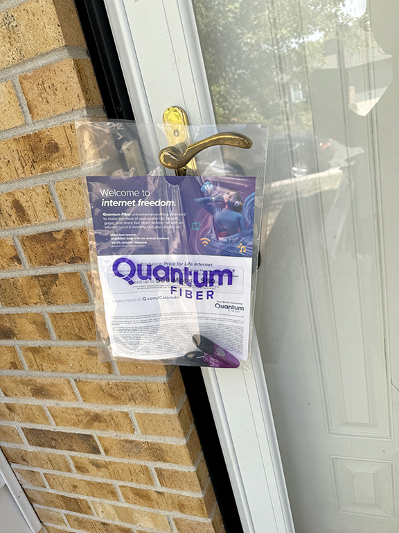 Door hanger advertising Quantum Fiber service, featuring a welcome message and promotional graphics, displayed on a residential door in Wyoming.