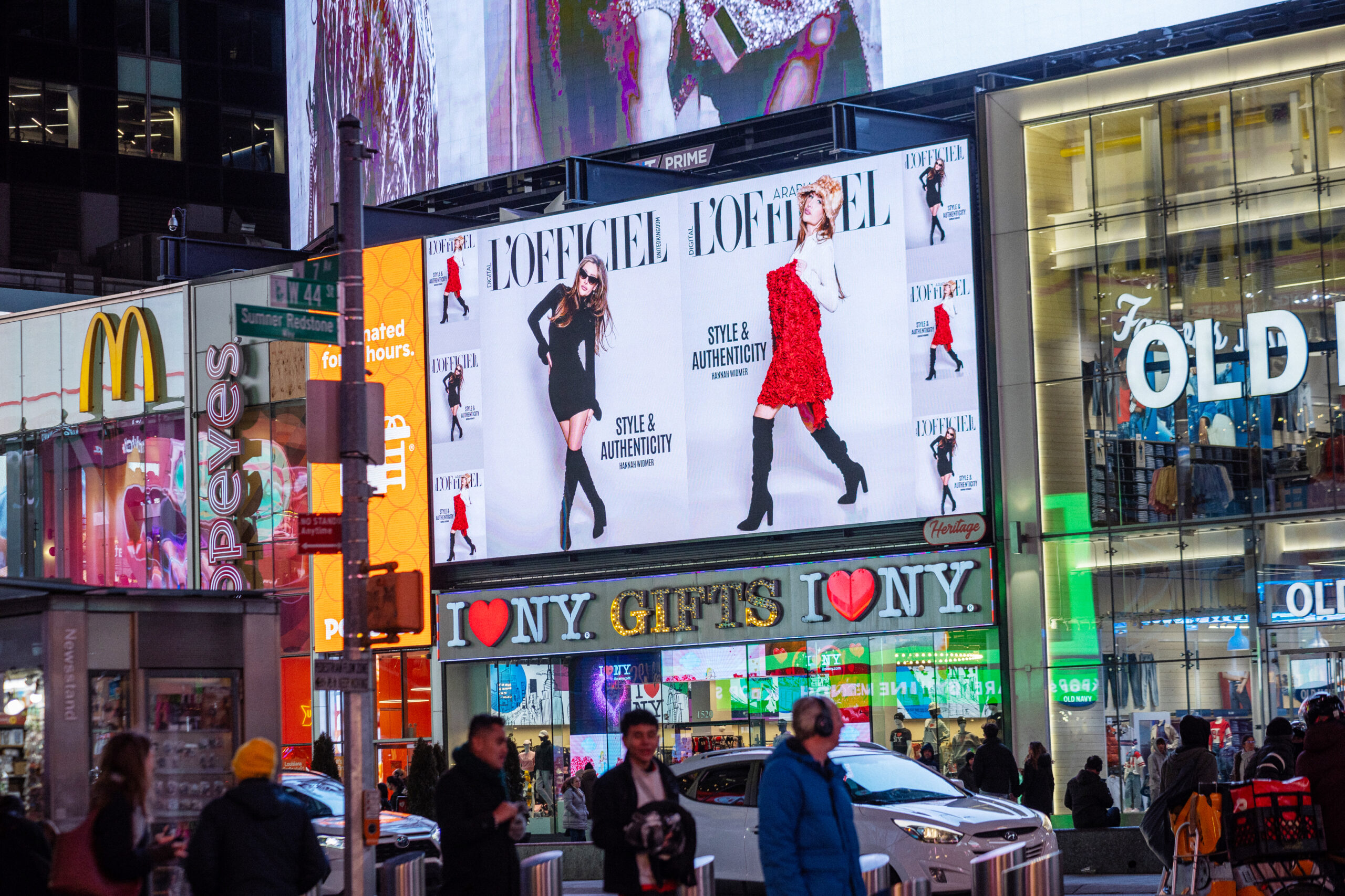 Billboard advertisement in Times Square featuring models showcasing fashion styles with the text "STYLE & AUTHENTICITY," surrounded by vibrant city lights and pedestrians.