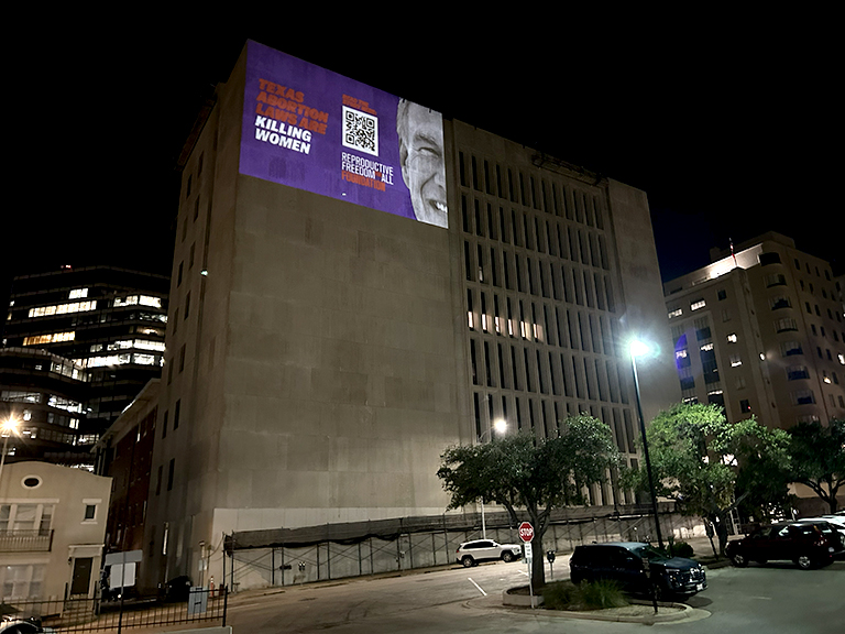 Projection mapping display on a building wall at night, featuring bold text "Texas is Killing Women" and a QR code, part of the Reproductive Freedom for All advocacy campaign in Austin, Texas.
