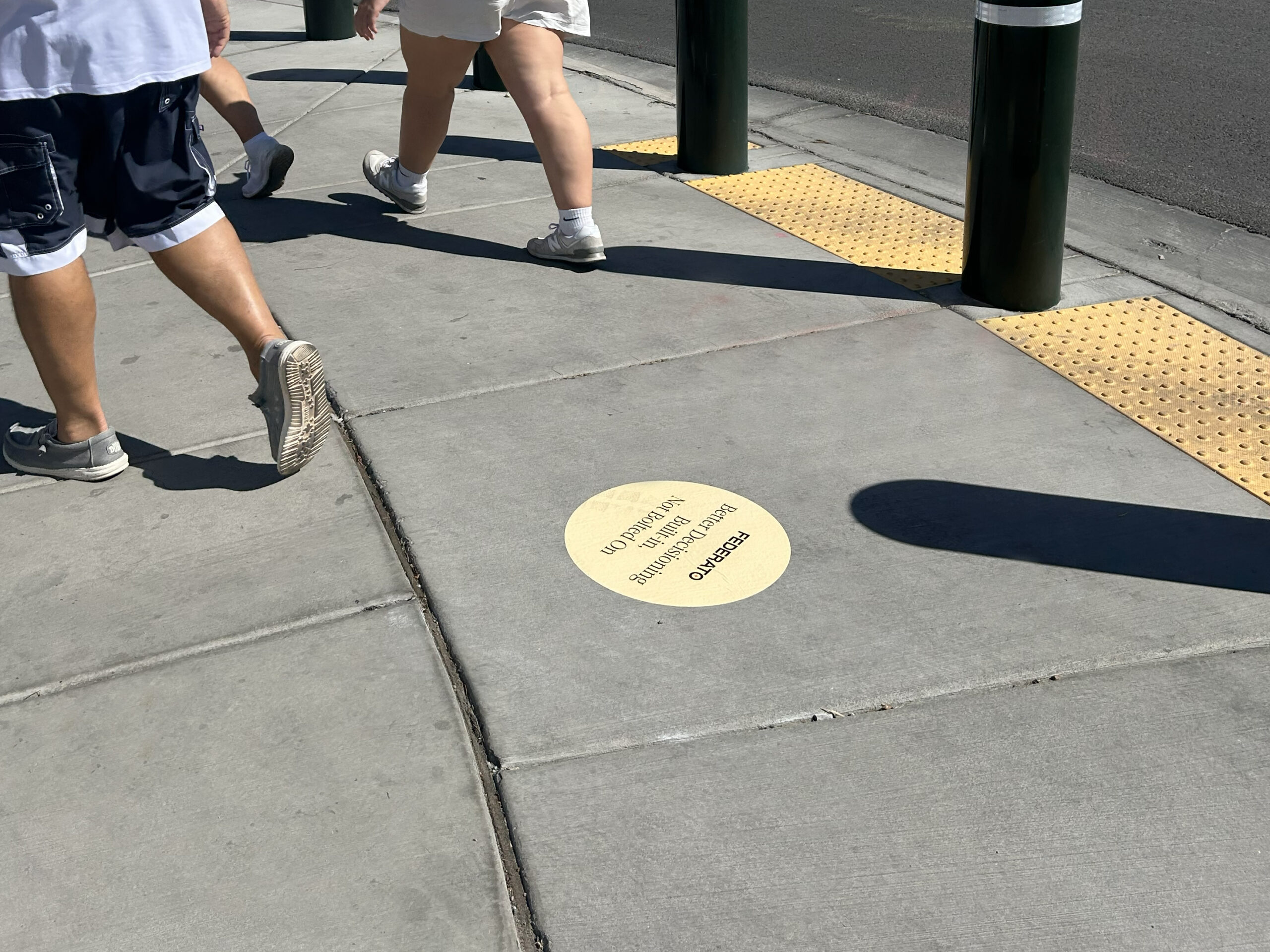 Sidewalk stencil advertising on a Texas street, featuring a circular design with promotional text, surrounded by pedestrians walking.