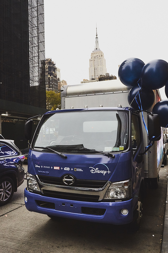 Disney+ LED billboard truck with promotional branding, balloons, and the Empire State Building in the background, Manhattan, New York.