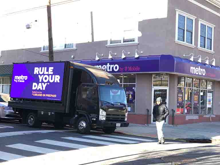 LED billboard truck for Metro by T-Mobile displaying "RULE YOUR DAY" advertisement in front of a Metro store, highlighting mobile advertising effectiveness.