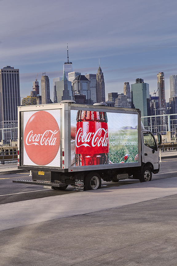 Coca-Cola LED billboard truck in Manhattan, showcasing vibrant advertisements with city skyline backdrop, emphasizing mobile marketing effectiveness.