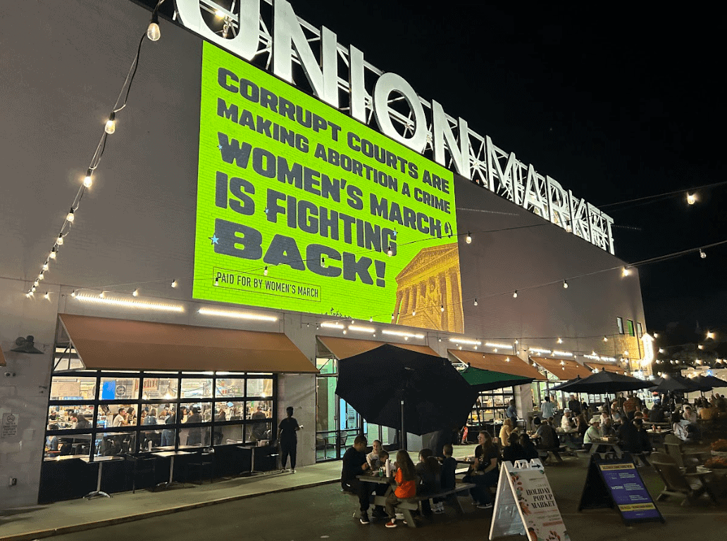 Projection advertising at Union Market, featuring a vibrant message about women's rights and activism, highlighting the Women's March with a bold call to action against corrupt courts.