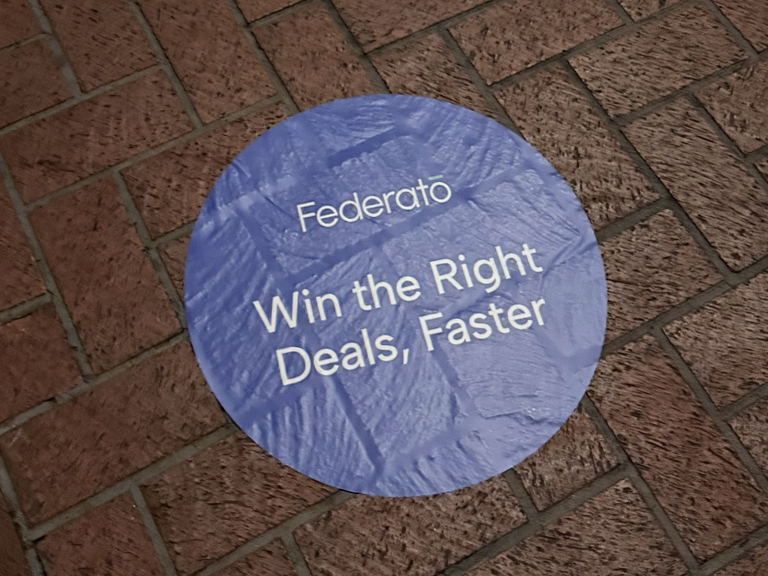 Circular sidewalk decal featuring the text "Federato" and the slogan "Win the Right Deals, Faster," set against a textured pavement background, showcasing outdoor advertising techniques for Federato in the Gaslamp District, San Diego.