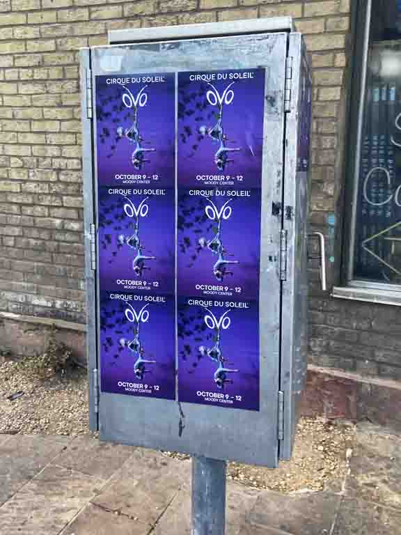 Posters for Cirque du Soleil's "OVO" promotion on a utility box, featuring event dates October 9-12, set in an urban environment.