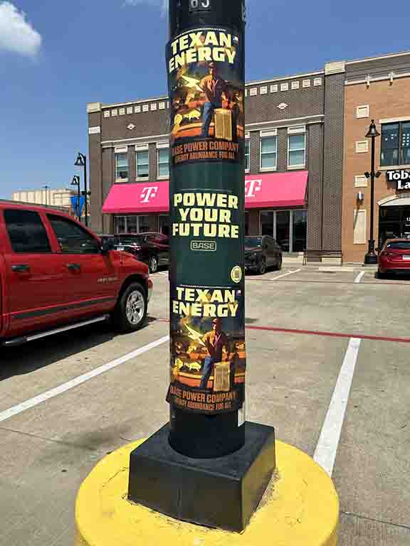 Texan Energy promotional posters on a pole, featuring "Power Your Future" tagline and BASE Power Company branding, in a commercial area with parked vehicles.
